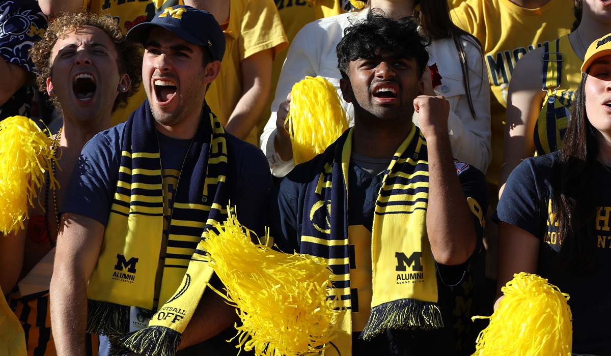 Fans dressed in maize and blue cheer at a Michigan football game