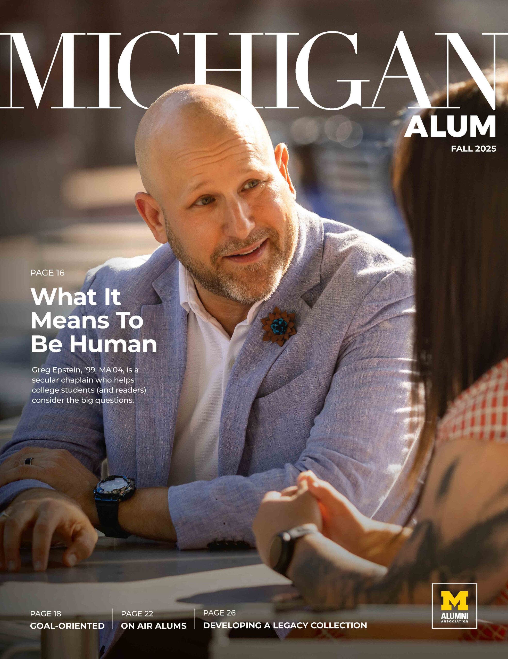 Cover of the Fall 2025 Michigan Alum magazine, which features two people at a table engaged in a conversation and the headline "What It Means To Be Human." Other story headlines are featured at the bottom.