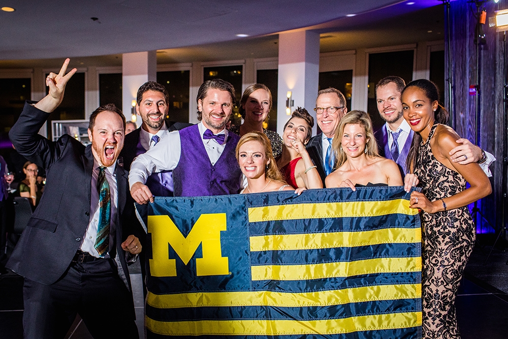 A photo from the wedding reception of Lisa Fetman, ’07, and Jerod Fetman, ’02. Some of the alumni wedding guests took a photo with a U-M flag, then proceeded to sing the fight song! From left to right: Robby Griswold, ’07, Aaron Saoud, ’09, Jerod Ryan, ’02, Lisa Feman, ’07, Nicole Kubon, ’07, MSW’09, Taryn Covrigaru, ’08, Robert Center, ’72, Cathryn Smeyers, ’04, Michael Pfeifer, ’01, BSN’06, ’07, Kimberly Pfeifer, ’05.