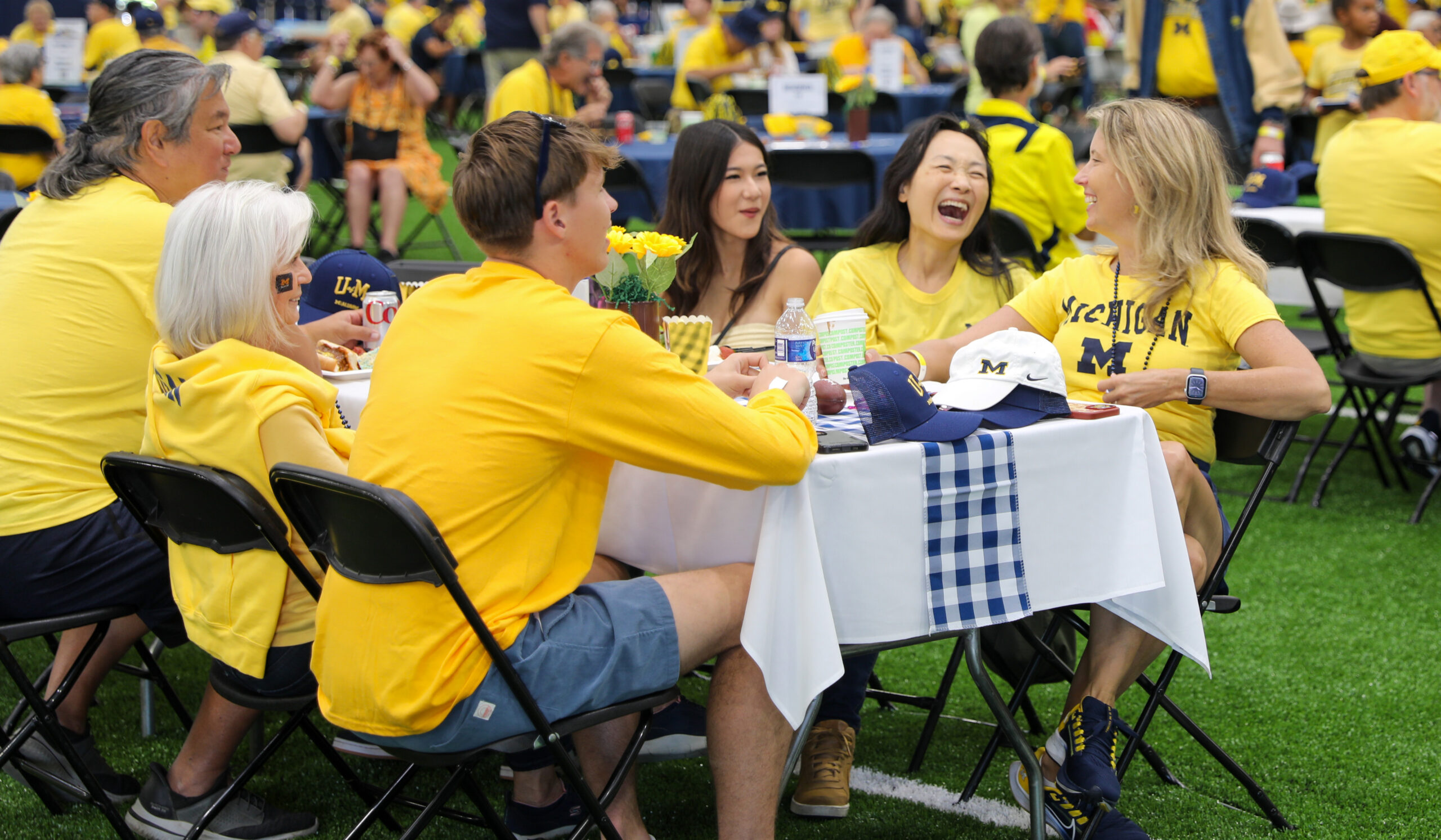 A group of people sit at a table wearing University of Michigan shirts and laugh.