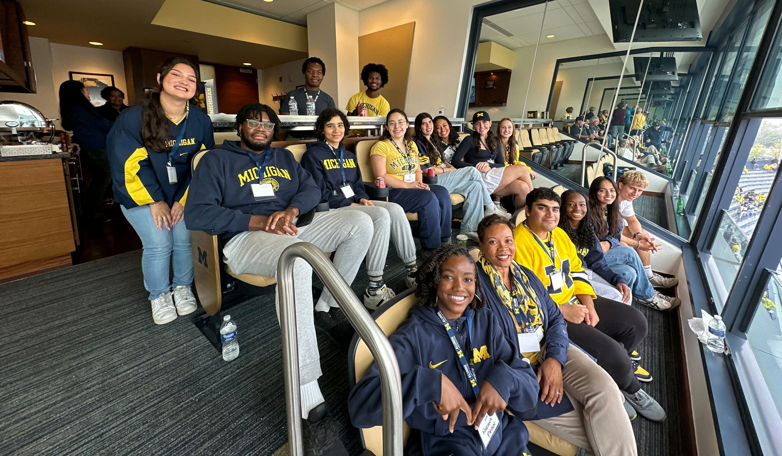 Students dressed in maize and blue watch a Michigan football game from a suite in Michigan Stadium with Alumni Association President and CEO Ayanna McConnell.