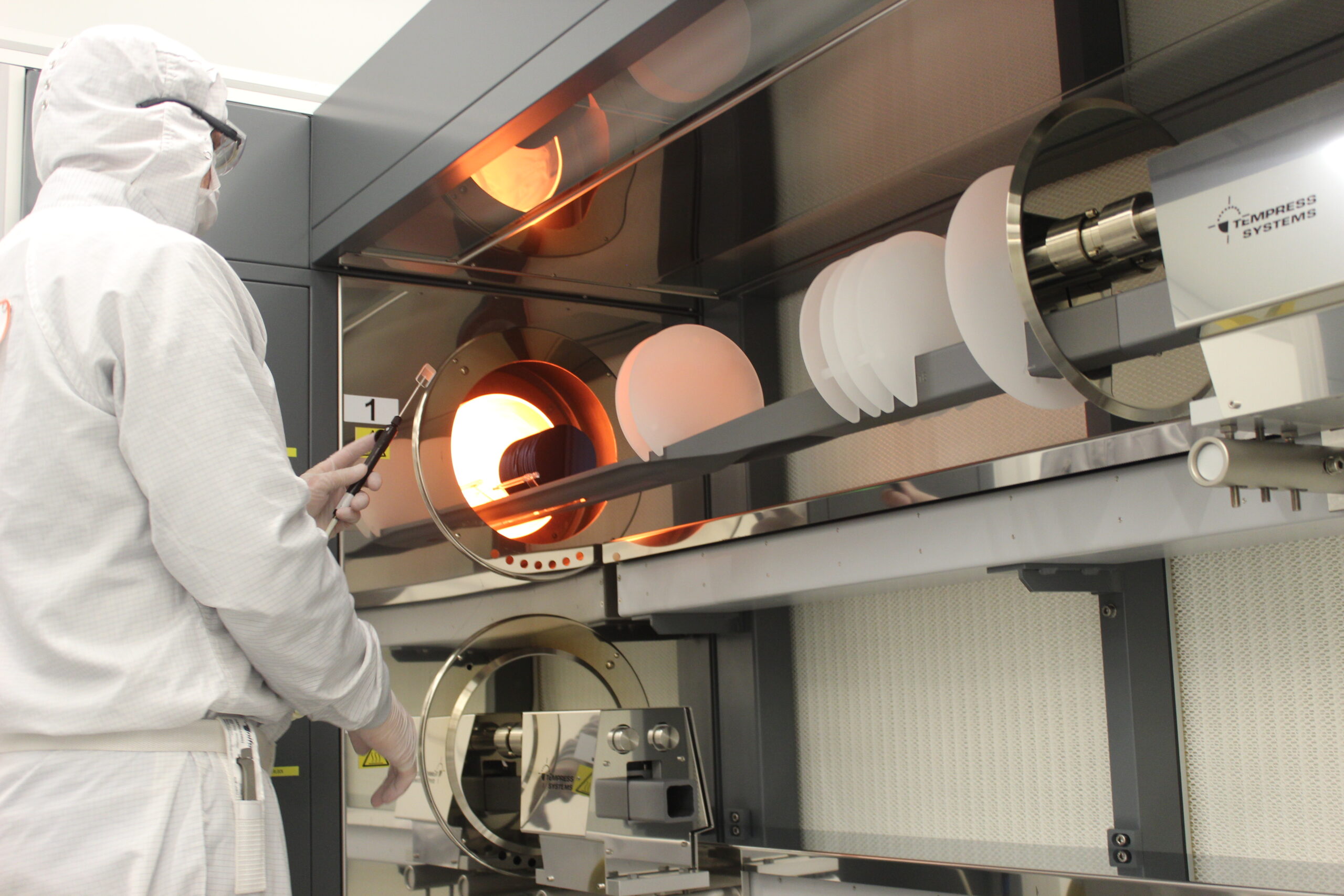 A person in a white clean suit uses equipment in the LNF.