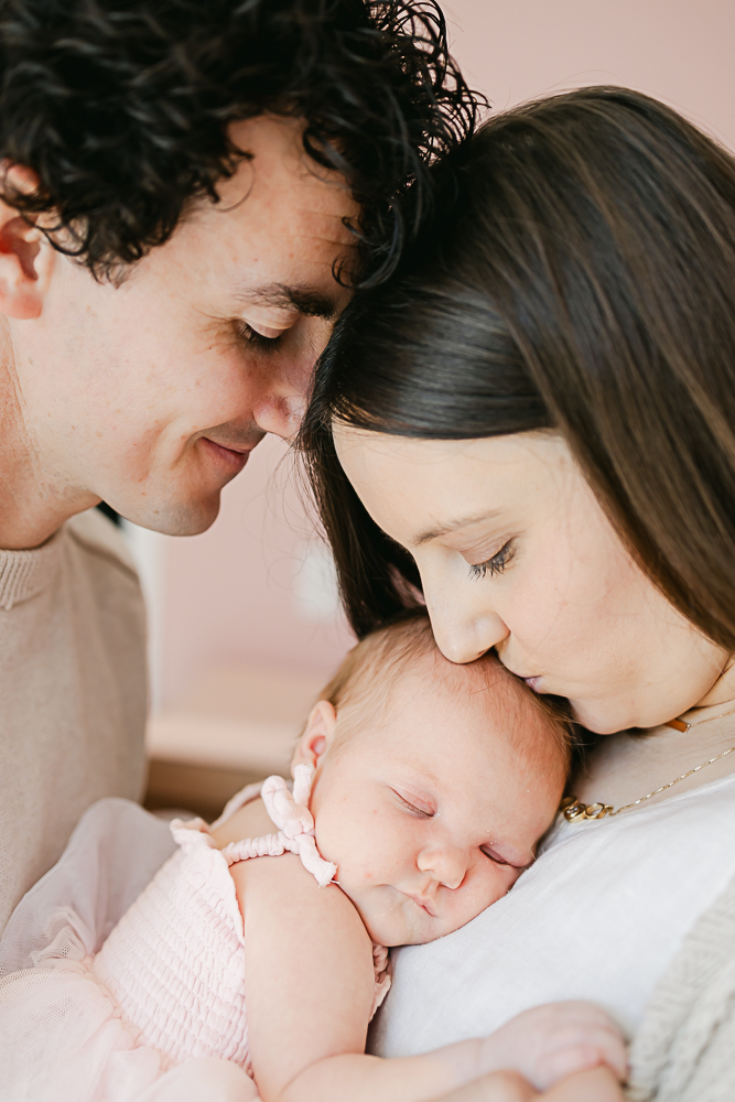 Ben (left) and Hannah (right) pose while holding their newborn daughter.