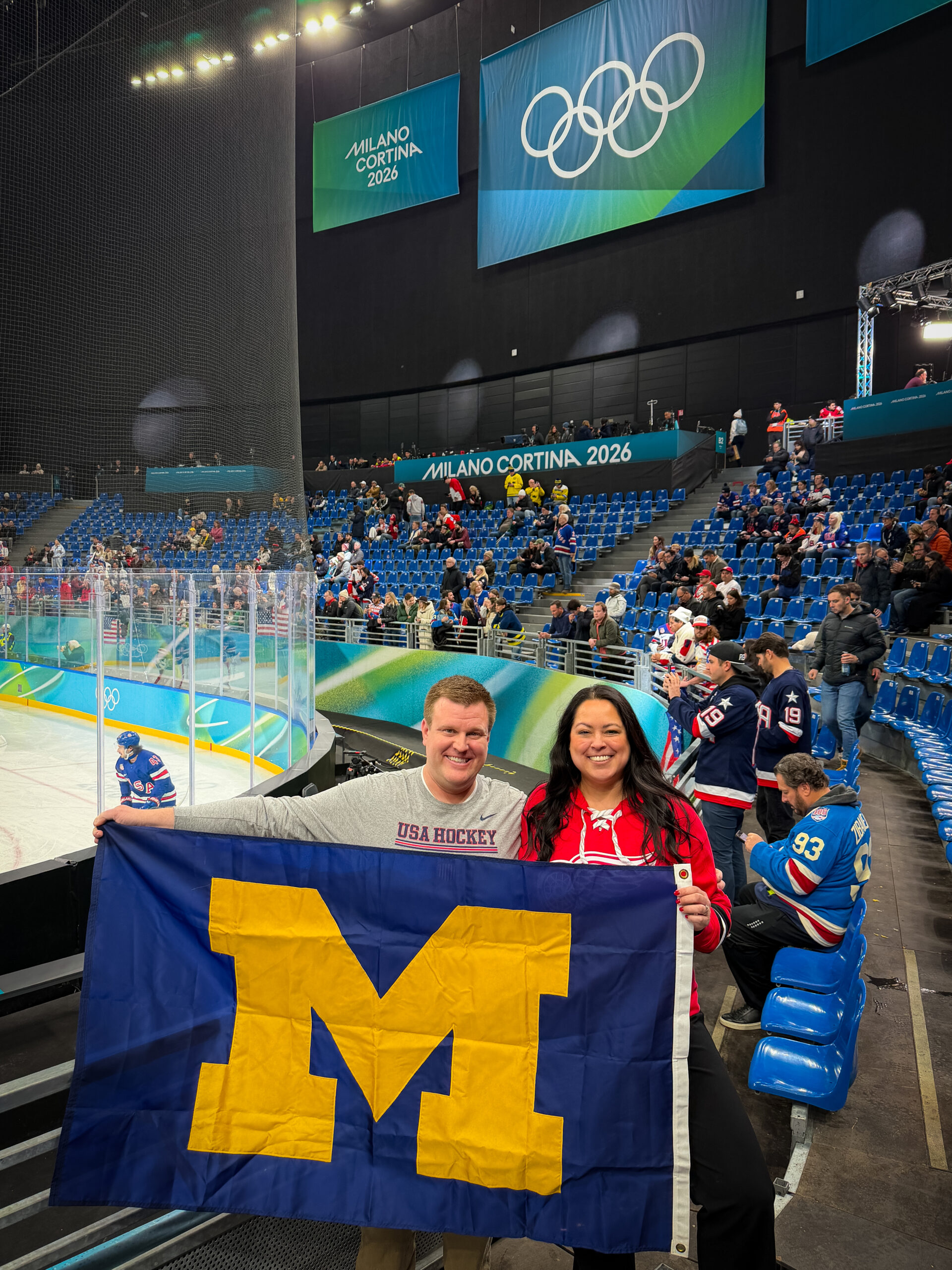 Austin and Meredith Chapman pose behind a Block M flag in an Olympic ice stadium