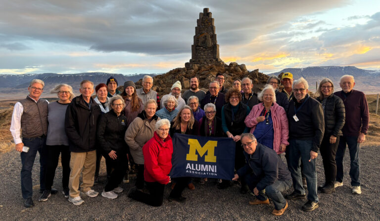 The Michigan Alumni Travel group poses for a photo with an Alumni Association flag.