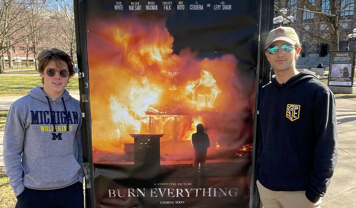 Jason Fine (right) and Caleb White (left) on the Diag in Ann Arbor, flanking a movie poster for "Burn It All"