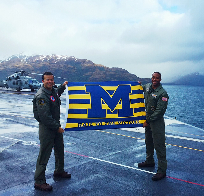 Lt. Cmdr. Carl E. Jones, ’07 (right), helps unfurl a U-M flag on the USS George Washington at the tip of South America in 2015.
