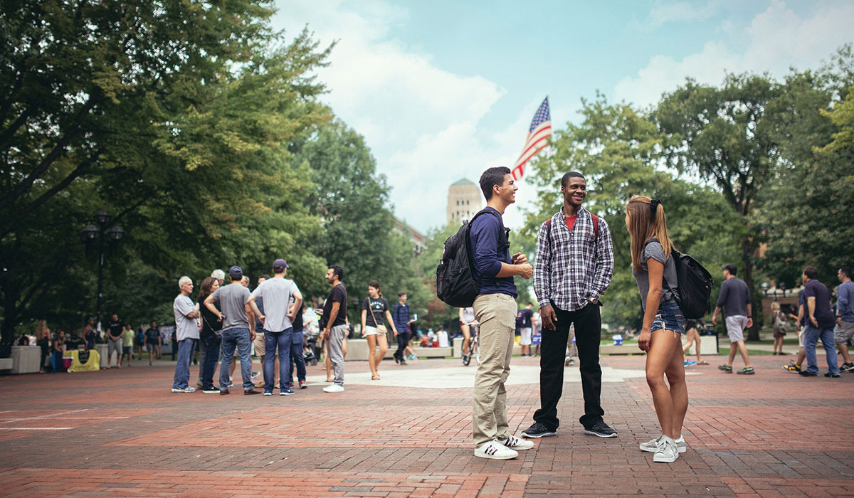 Groups of people stop and chat in the Diag at the University of Michigan.