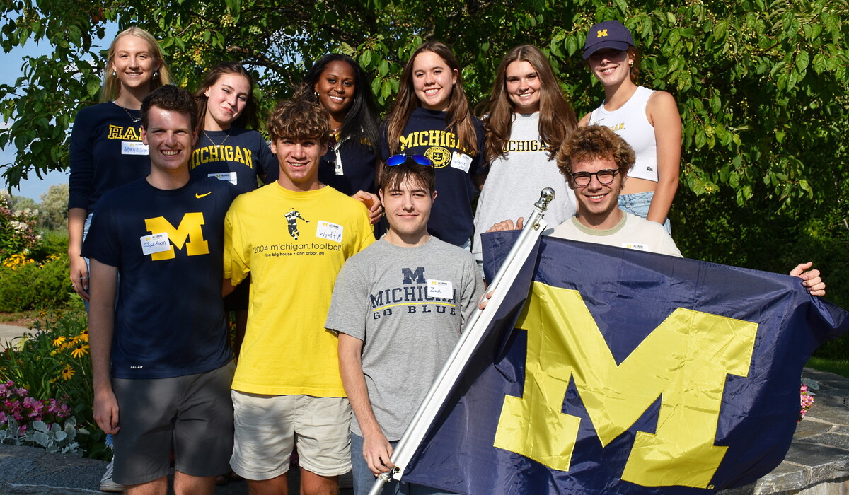 Students pose with a large blue and maize U-M flag.