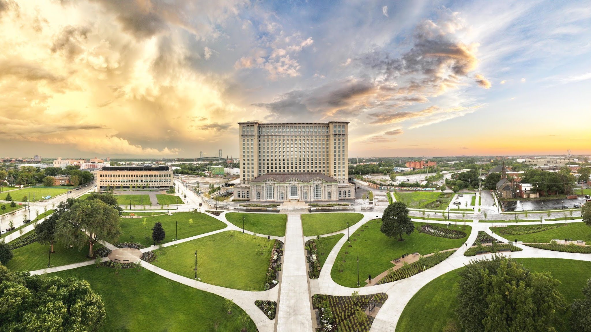 A wide image of Michigan Central Station and the park around it, with green grass and lots of walking paths.