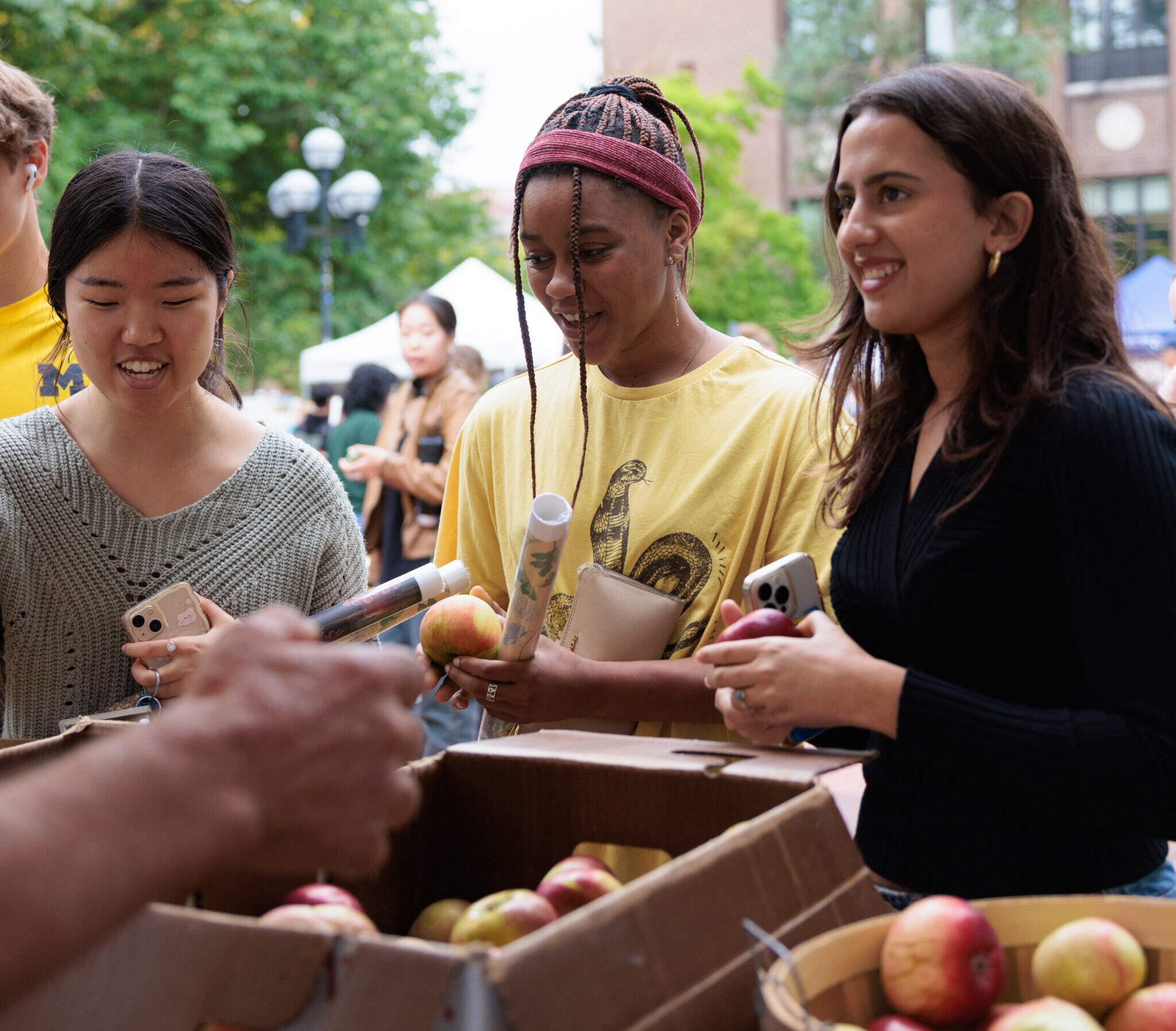 Three students accept free apples from one of the vendors on the Diag.