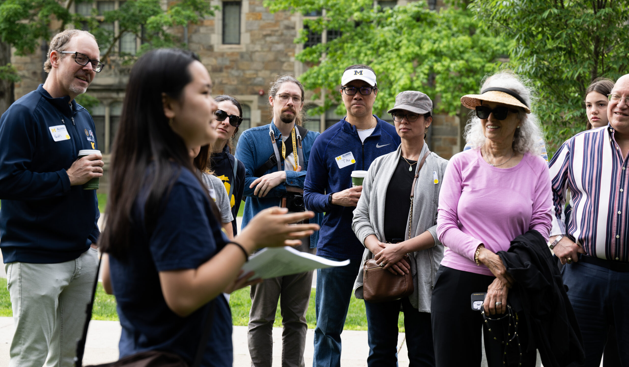 A person with long dark hair speaks to a group of alumni gathered on campus.