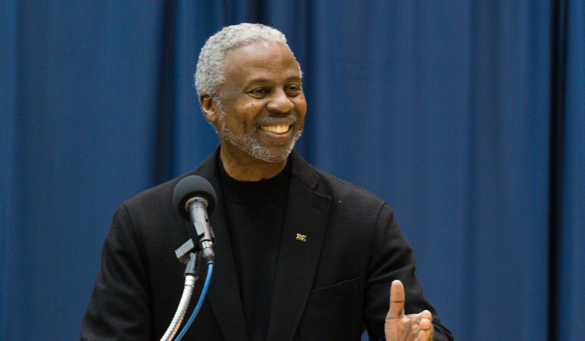 A Black man with gray hair smiles as he speaks at a podium.