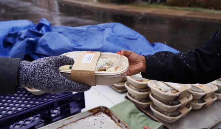 Photo, focused on the hands, of a Make Food Not Waste worker handing off a prepared meal to another person