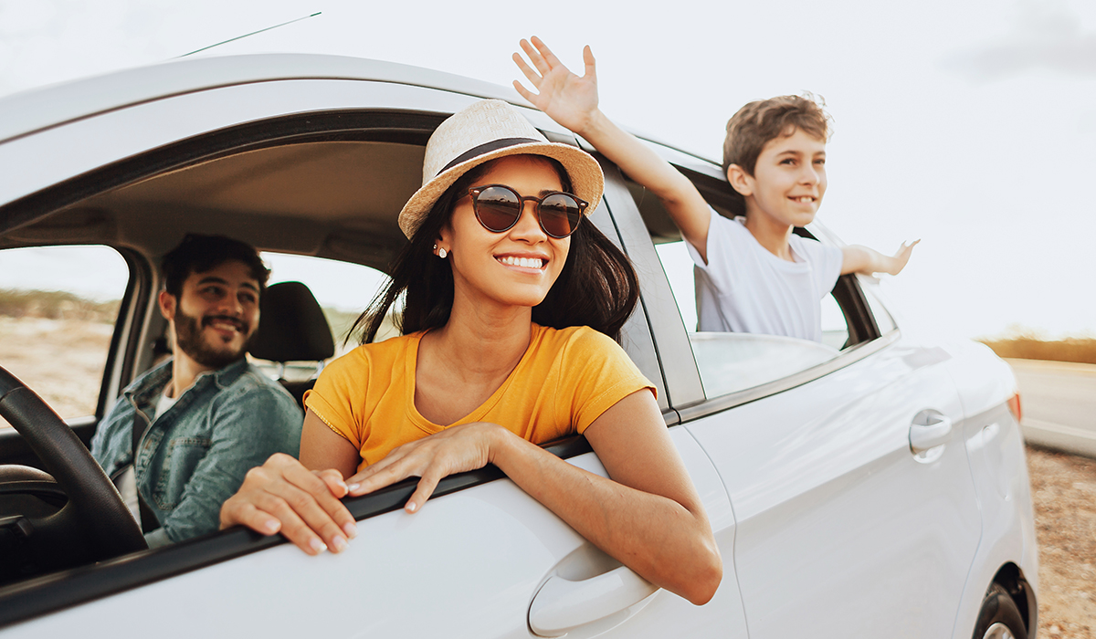 A family smiles as they look out the open windows of a car