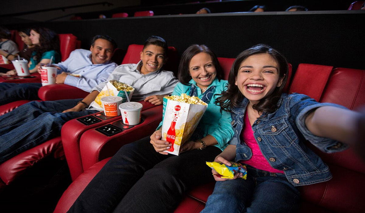 A family takes a selfie while seated in a movie theater.