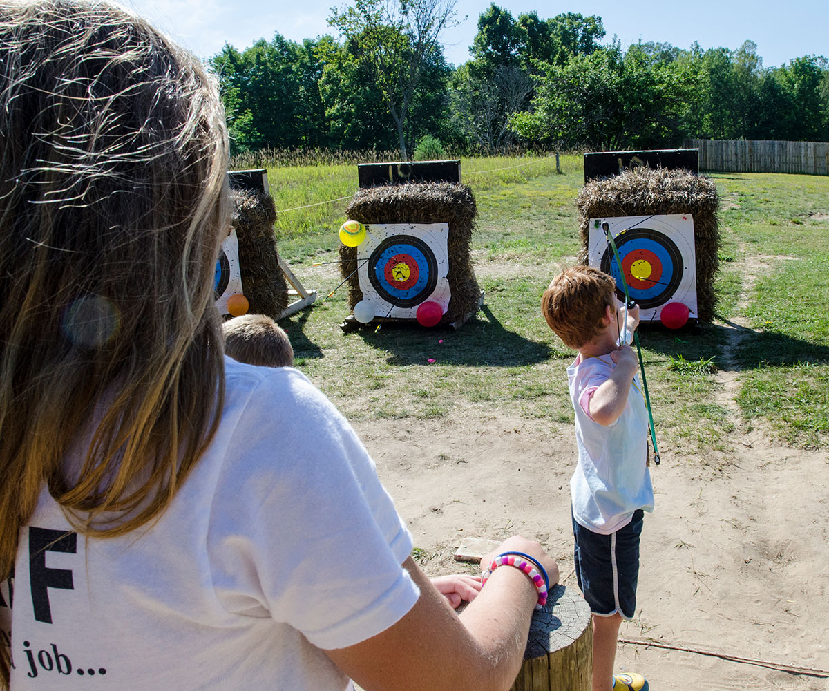 A child shoots an arrow at the archery range at Camp Michigania as a staffer looks on