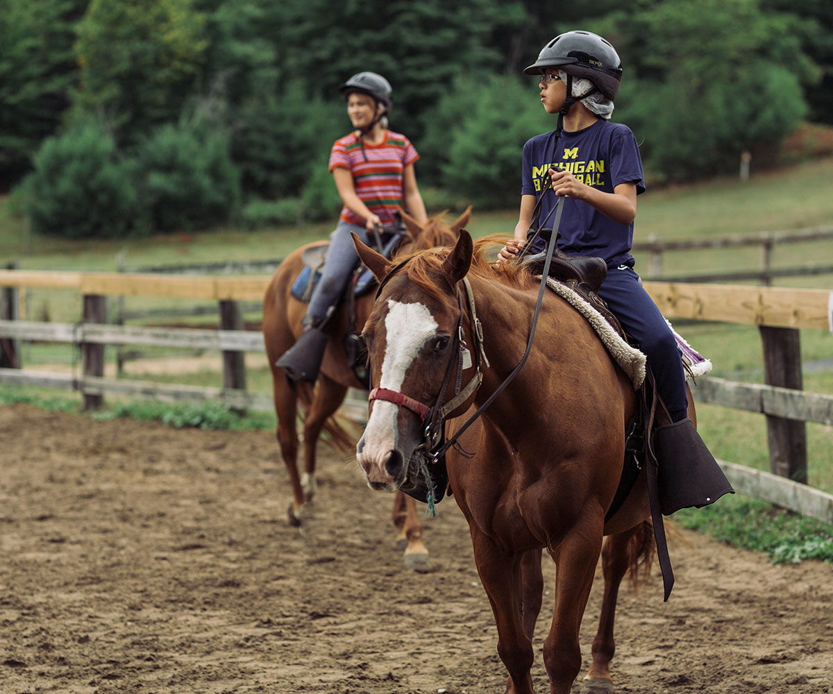 Two people ride horses at Camp Michigania