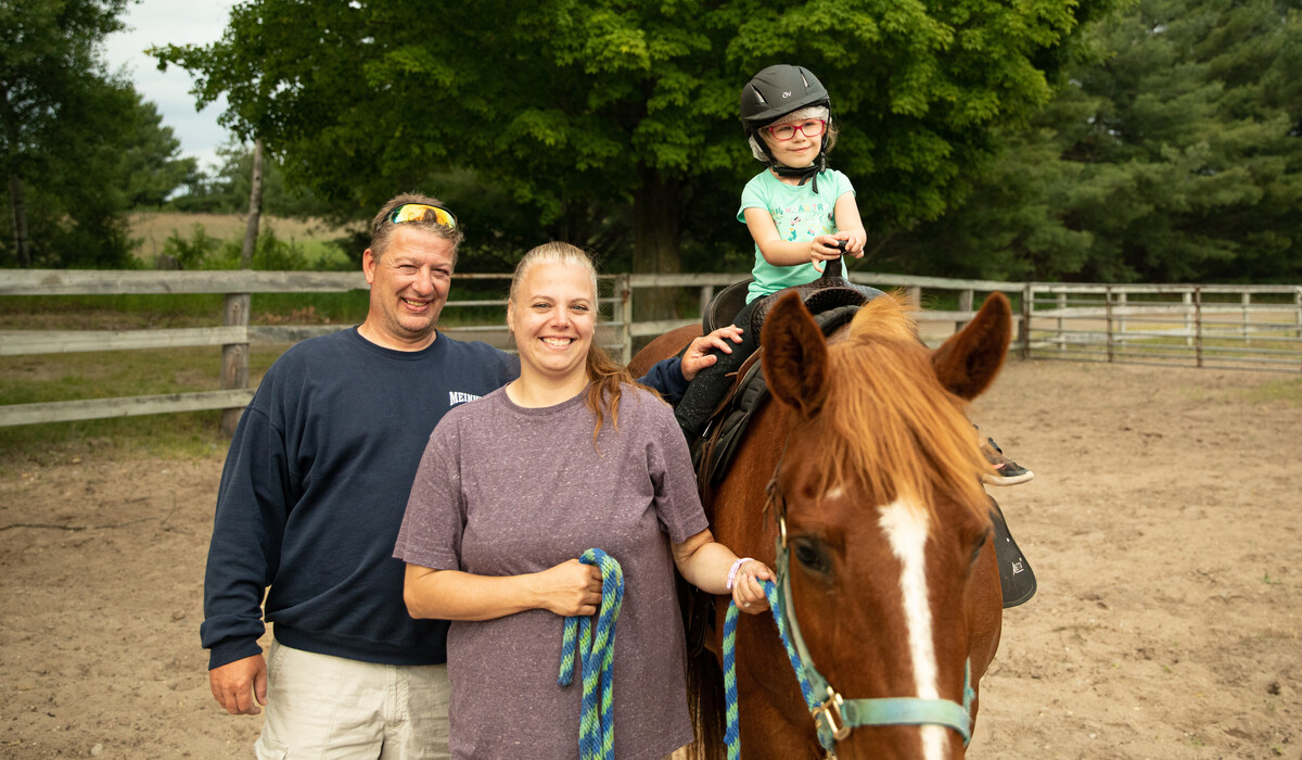 A mother and father pose with their daughter who is sitting on a horse at Camp Michigania.