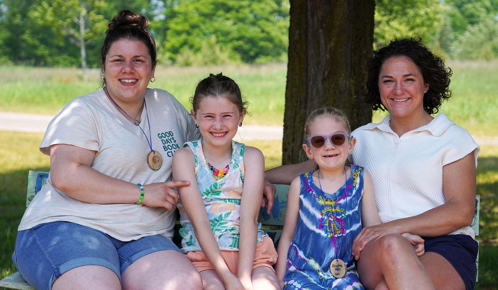 Two adults and two children pose for a photo on a bench in front of a tree at Camp Michigania.