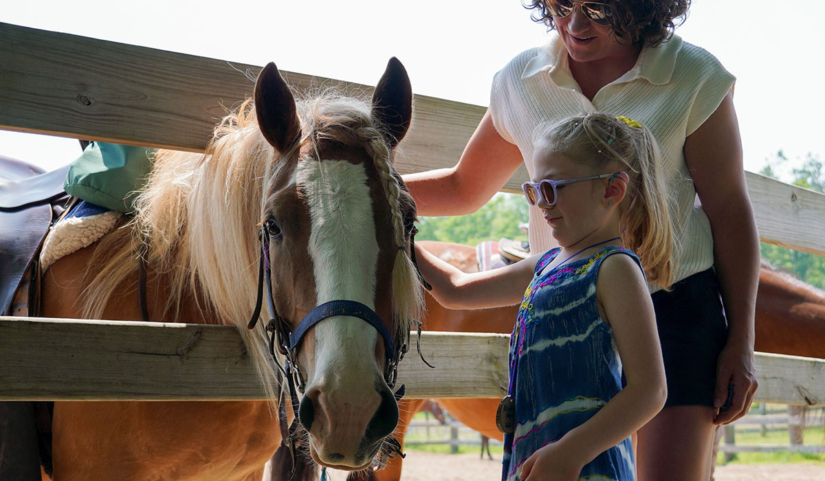 A child and an adult pet a horse at Camp Michigania.