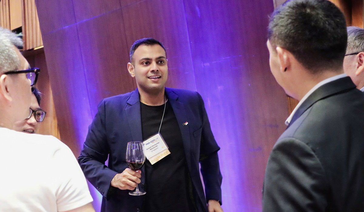 A person walks toward a group while holding a wine glass at the 2025 Pan-Asia Alumni Reunion.