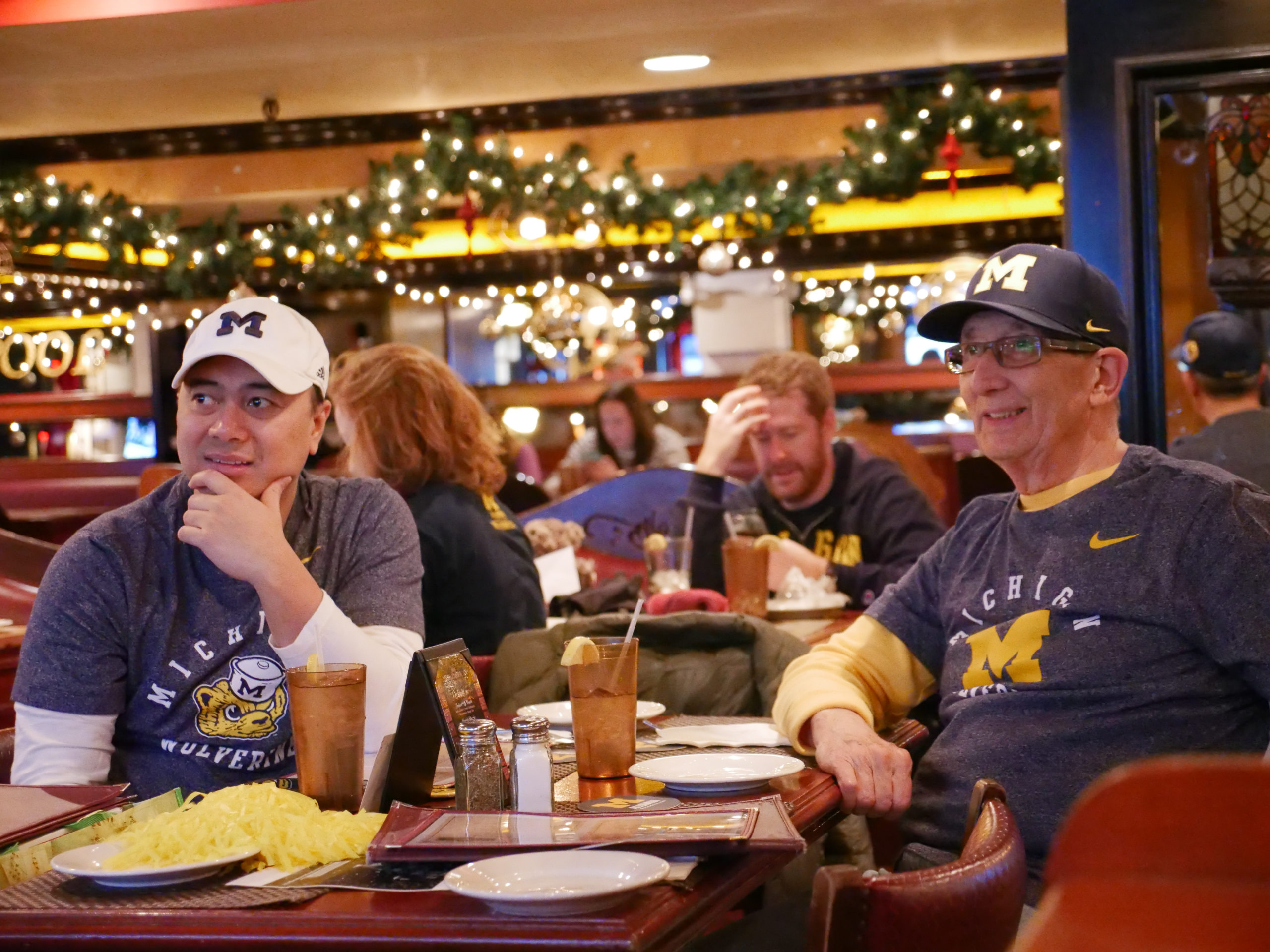 Two men in U-M clothing sit at a restaurant table at a watch party