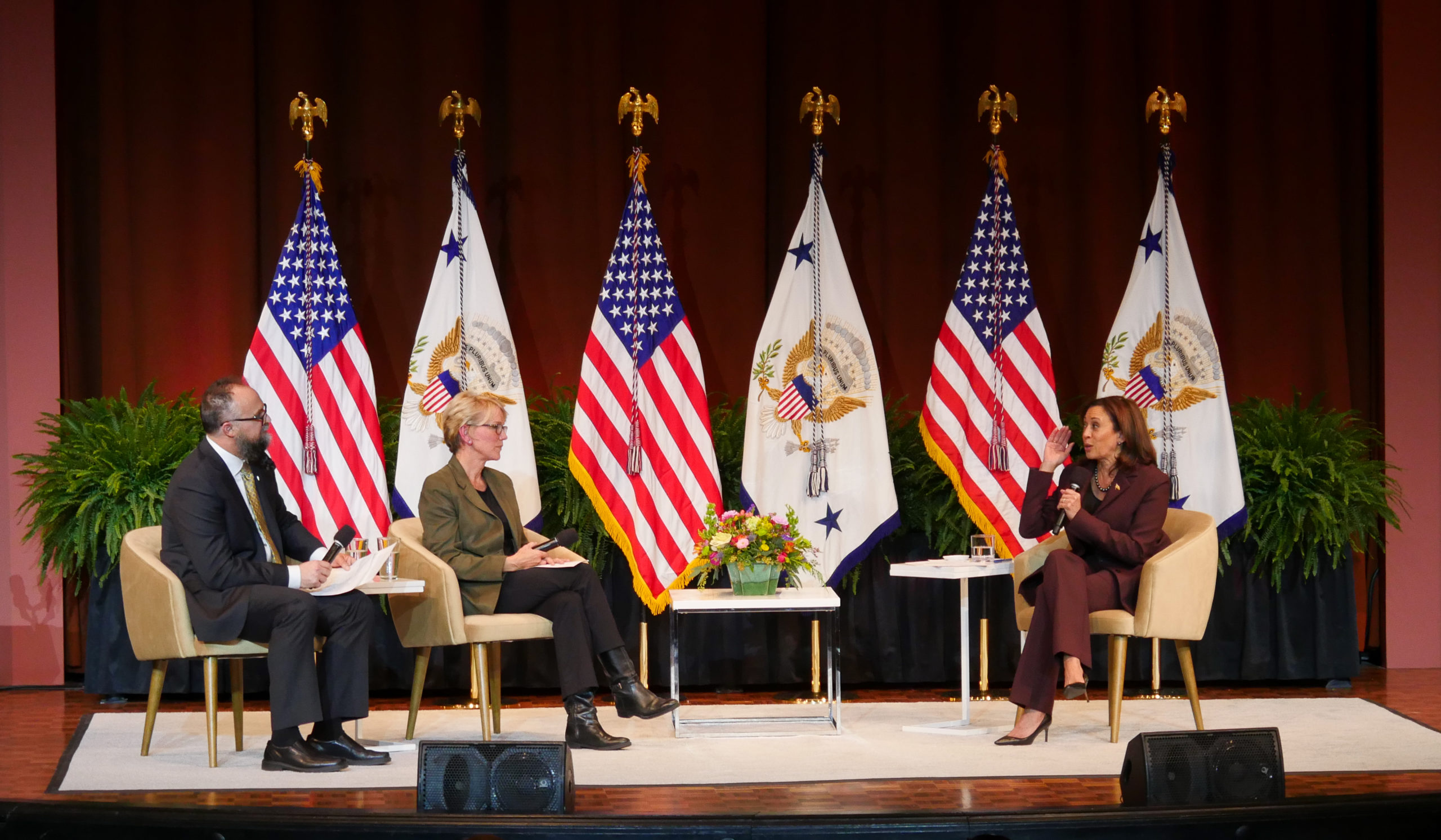 (From left to right) U-M professor Kyle Wright and Secretary of US Department of Energy Jennifer Granholm moderate a conversation with Vice President Kamala Harris. The stage is set with flags behind the speakers.