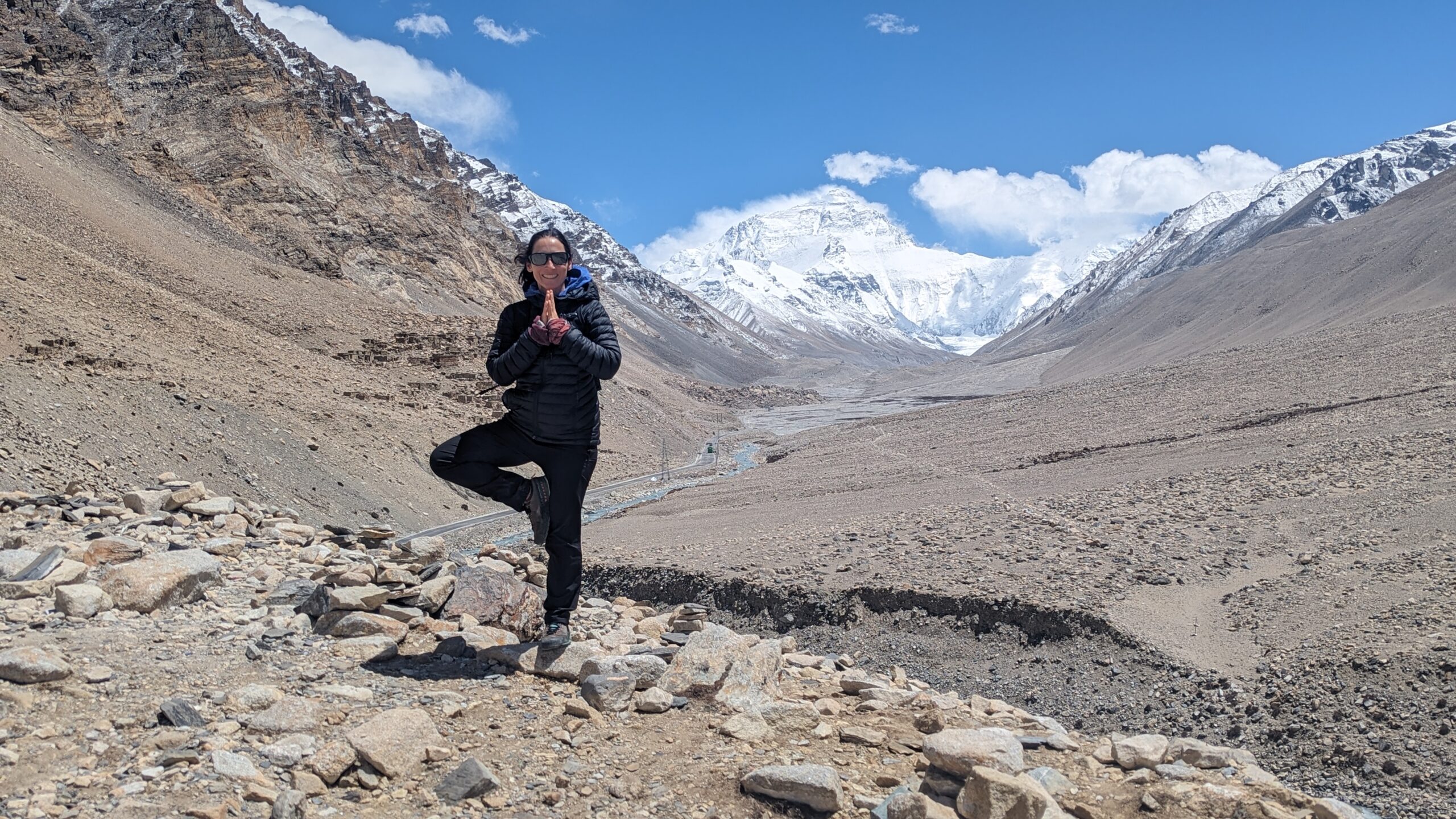 Myra does a tree yoga pose on rocky terrain with a snowy Everest in the far background.