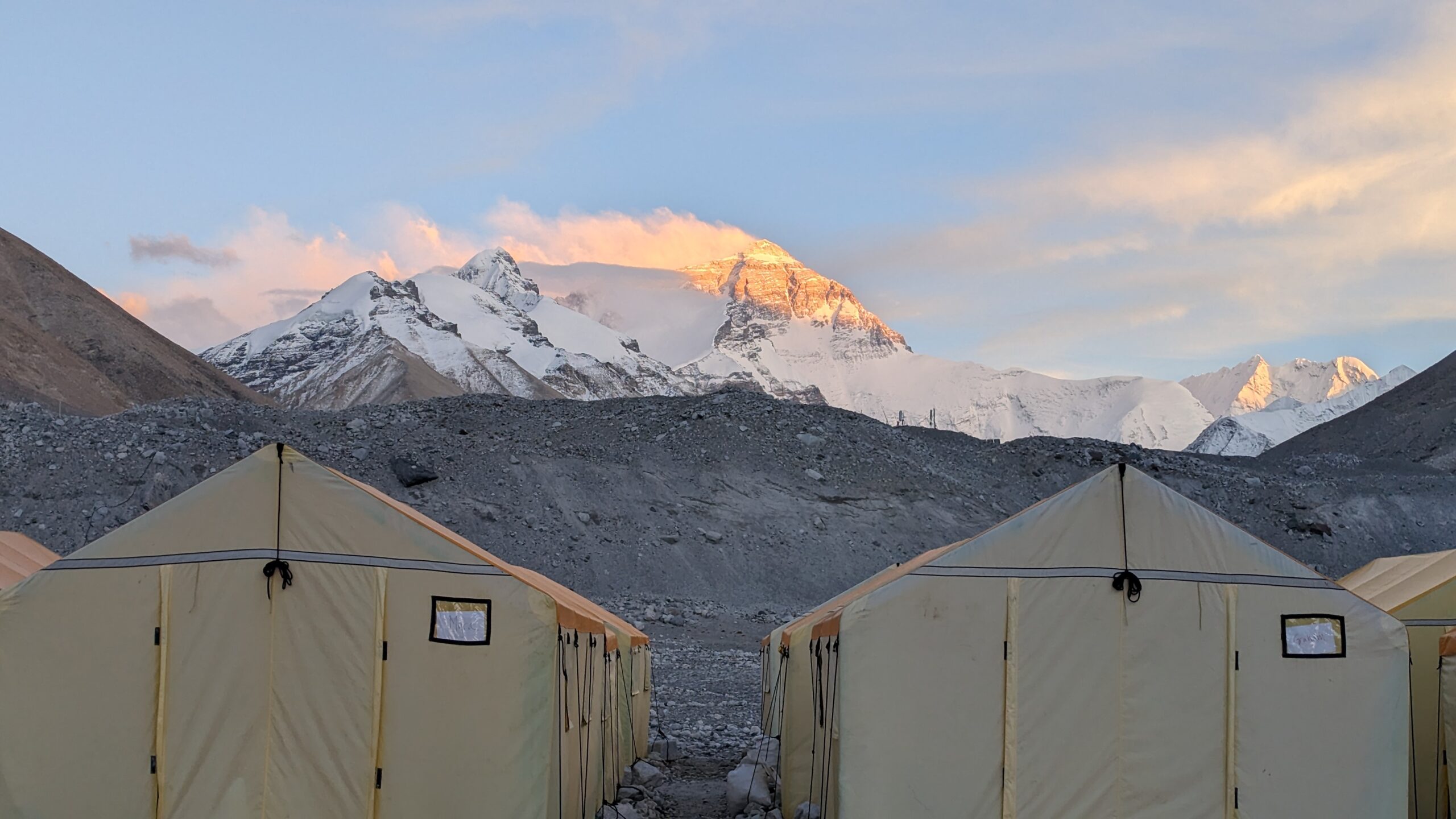 Beige tents at Everest Base Camp with the sun illuminating the snowy top of Everest.