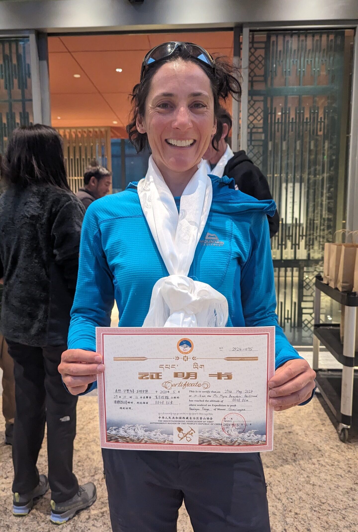 Myra Beaudoin Bertrand in a blue shirt holding a certificate that is written in a foreign language.