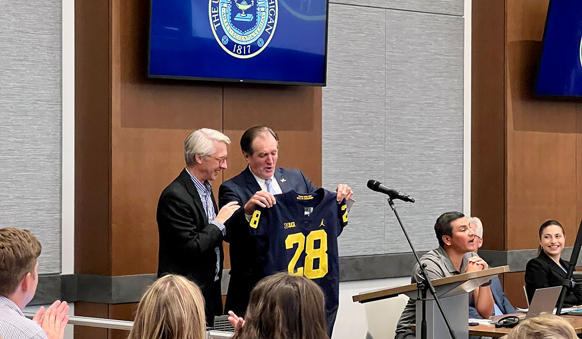 Regent Paul Brown presents a Michigan football jersey with the No. 28 to Alumni Association president and CEO Steve Grafton