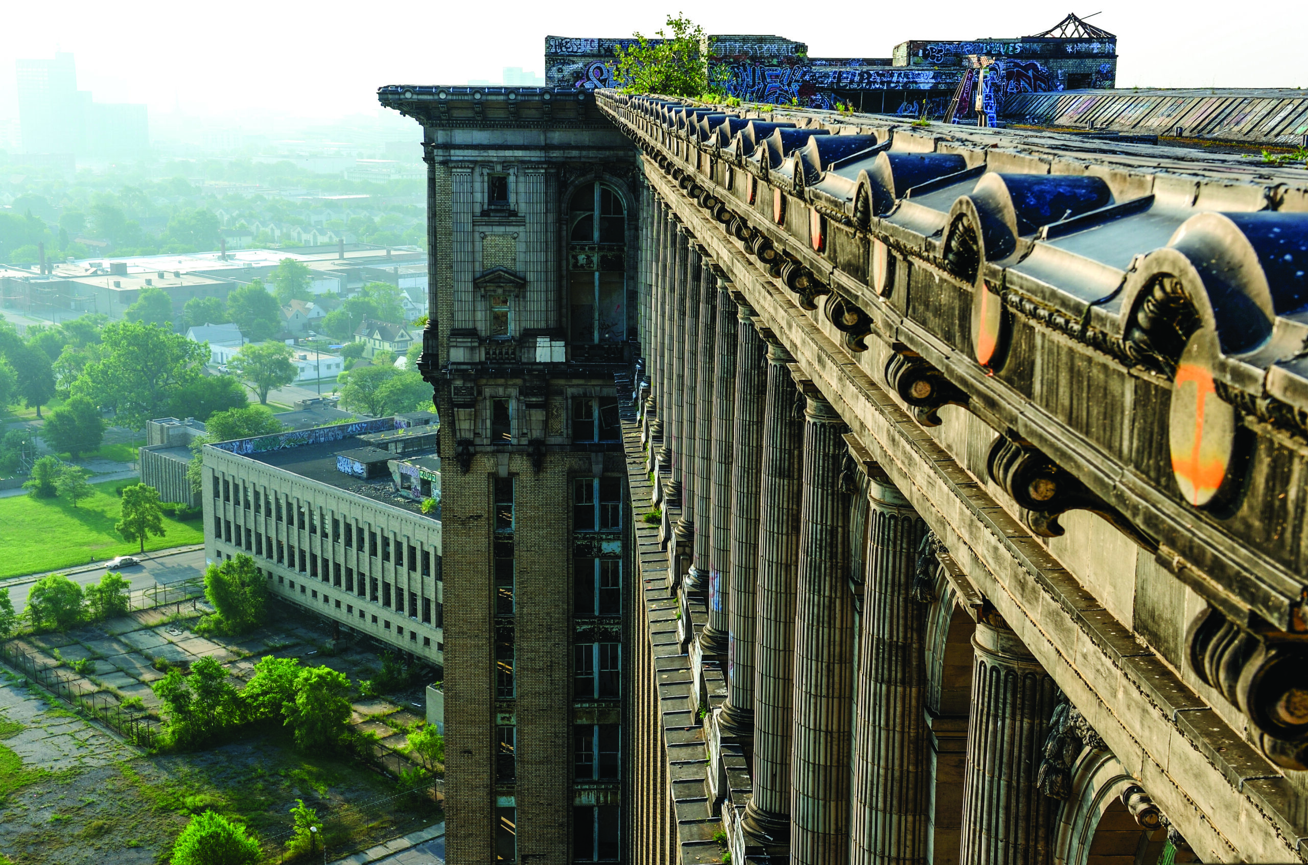 A picture of the roof line of Michigan Central Station with graffiti and weeds.