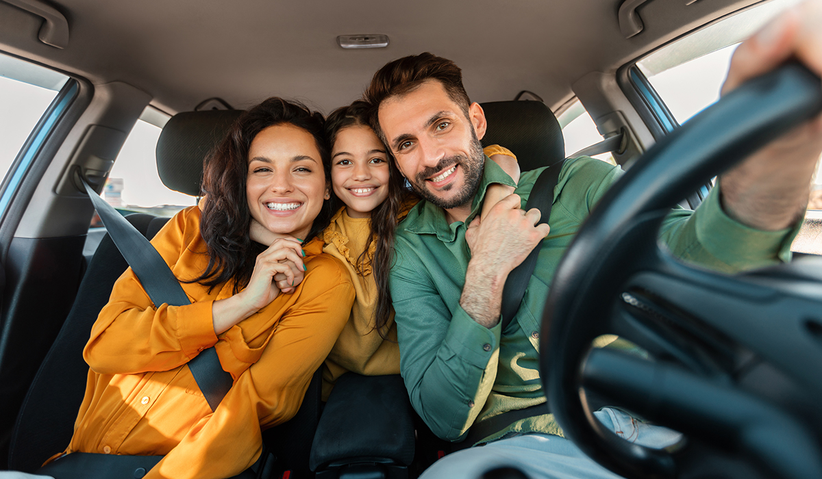 A family of three smiles for a group photo while sitting in a car.