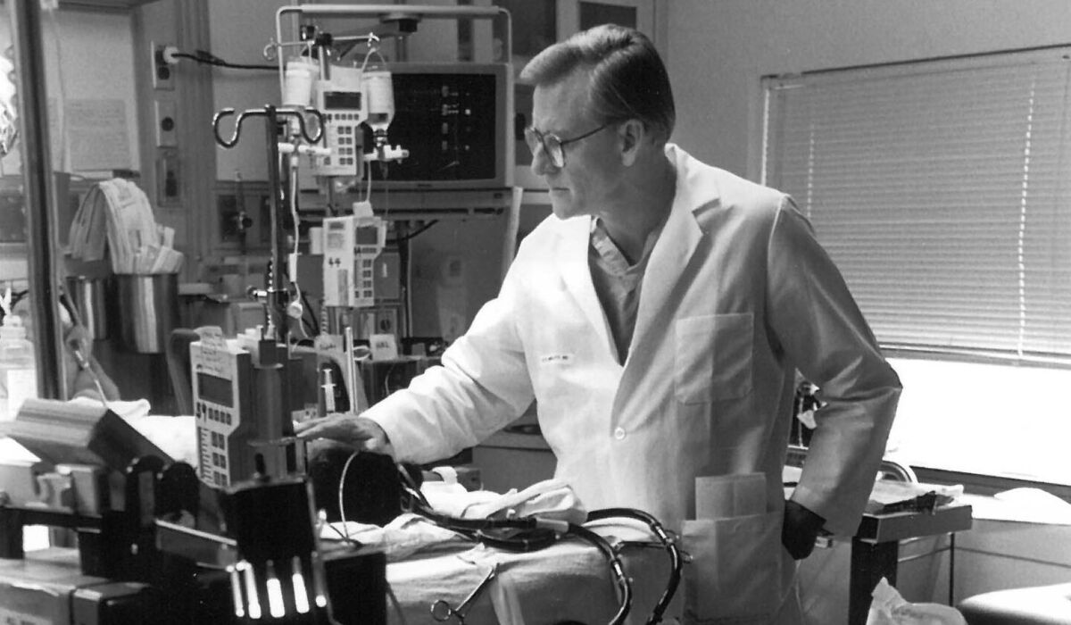 Black-and-white photo of ROBERT H. BARTLETT, MD’63, in a hospital room examining medical equipment