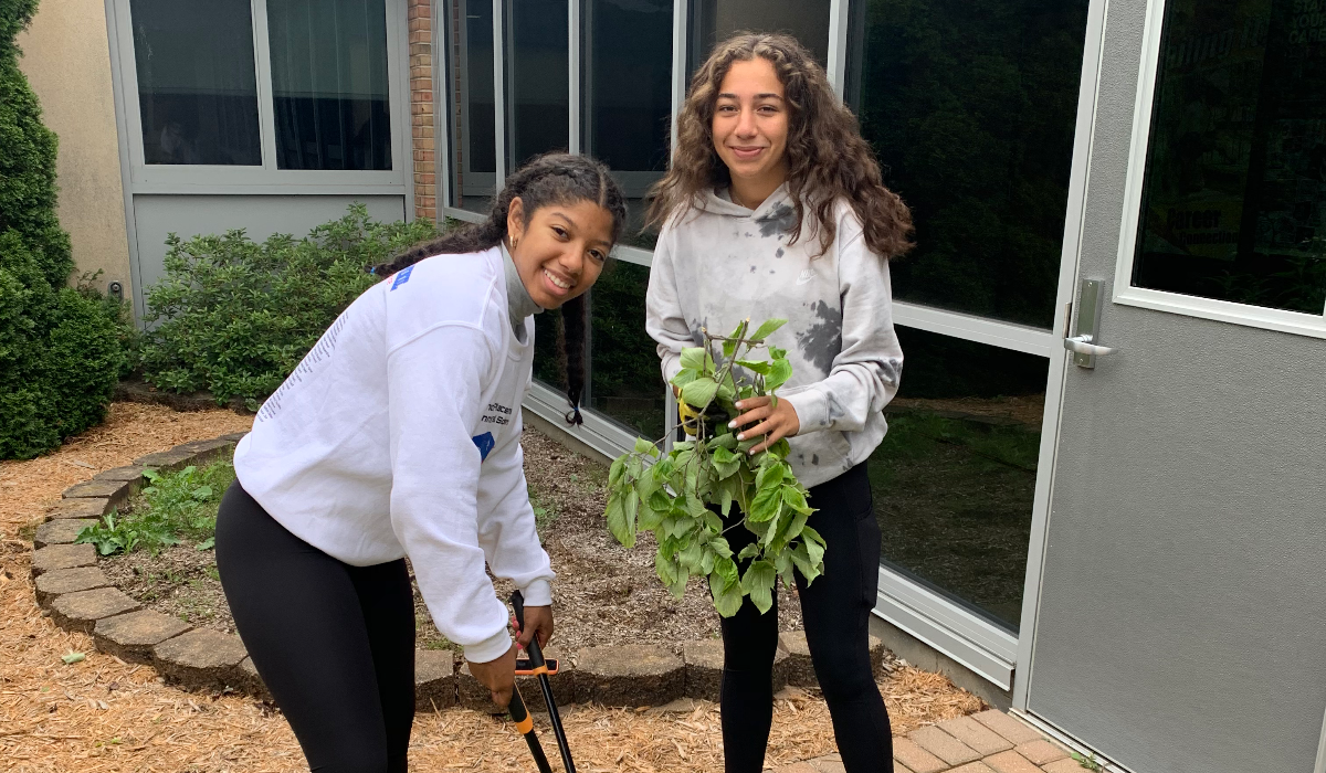 Sohair Holman (left) poses with a pair of trimming sheers. Another young person poses on her right with a bundle of leaves and twigs.