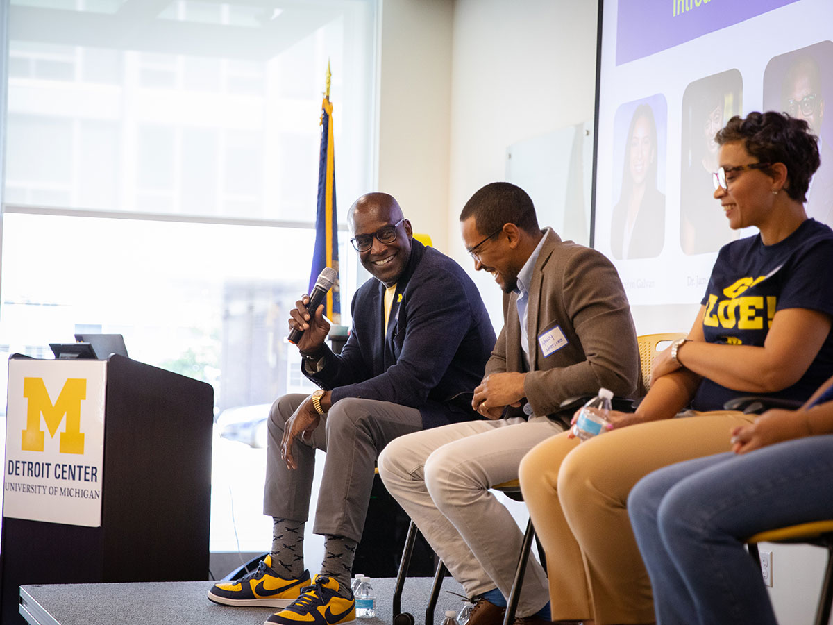 Three people smile during a panel discussion at the University of Michigan Detroit Center.