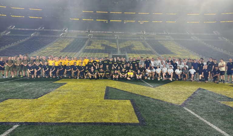 A large group of ROTC alums and current ROTC students pose at night on the field of Michigan Stadium.