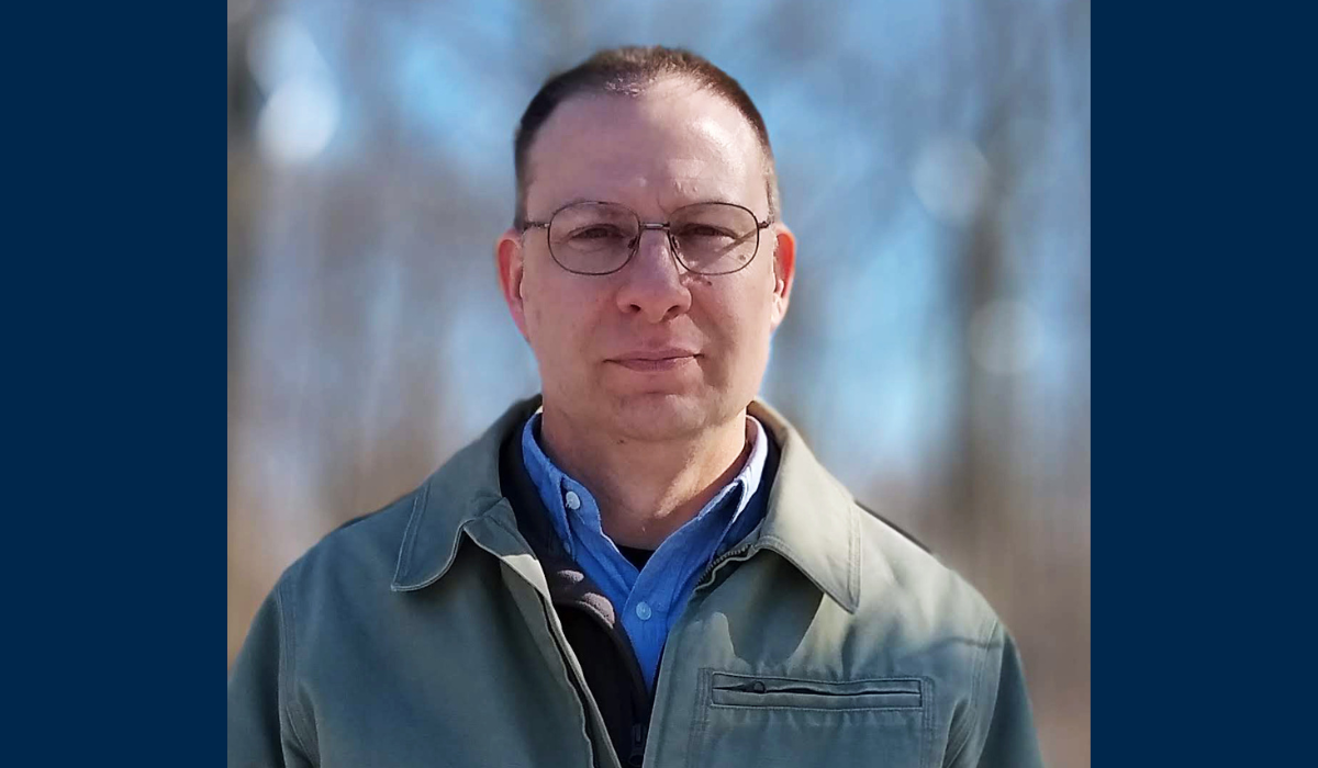 A headshot of the author outdoors with a blurred background. He has short hair and is wearing glasses.