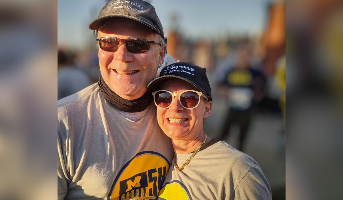 Bill and Susan, both wearing Laurentide hats and Big House 5k shirts, pose for a selfie.