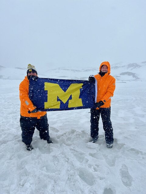 James Valk, DDS’79, his wife, Diana (behind the camera), and their son, Evan, ’14, MBA’21, flew the U-M flag during a blizzard on Deception Island, Antartica, the morning of the Wolverines vs Buckeyes football game in November 2023.