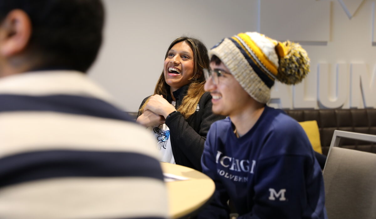 Two students, a male and female, laugh while looking forward. The male student is wearing a University of Michigan stocking hat.