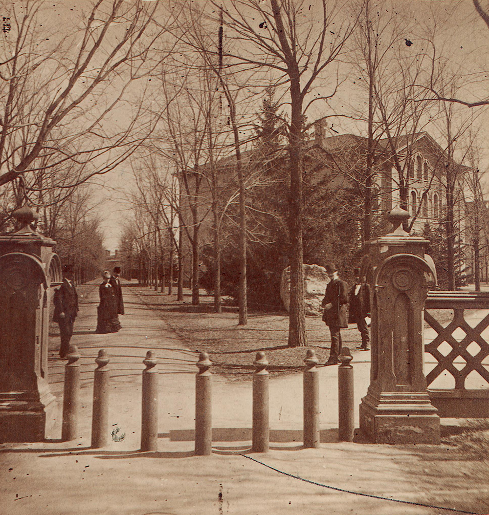 Students go for a stroll in 1888 near the main entrance of U-M and close to the northwest corner of the Diag. To the right are Law School buildings.