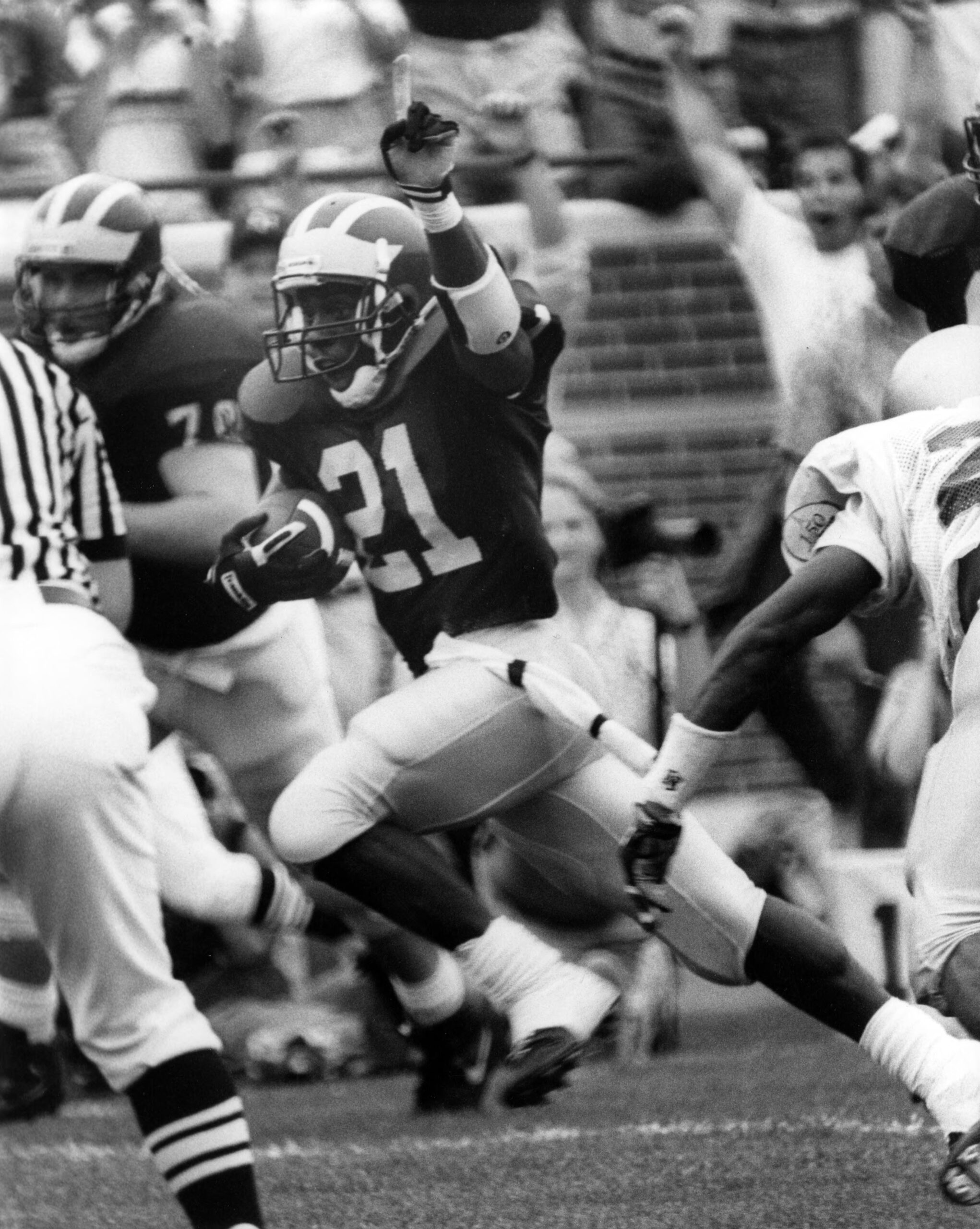 Black and white photo of Desmond Howard, wearing the number 21, in a football game, running with the ball in his right hand.