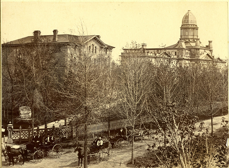 1873: True “horsepower” was the transportation of choice on campus before automobiles were widely available. (Ford’s Model T began mass production in 1913.) Here, horse-drawn carriages trot down State Street, passing the original Law Building (left) and University Hall.
