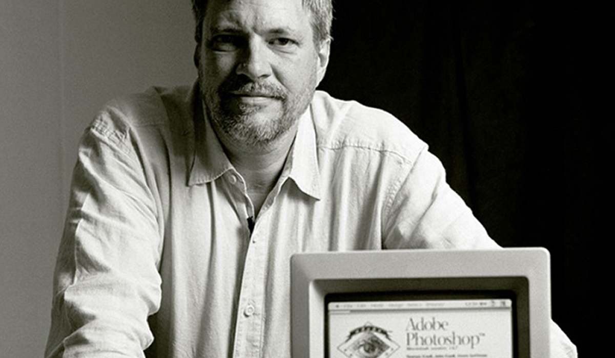 Thomas Knoll, posed behind an older model computer displaying an early version of Photoshop