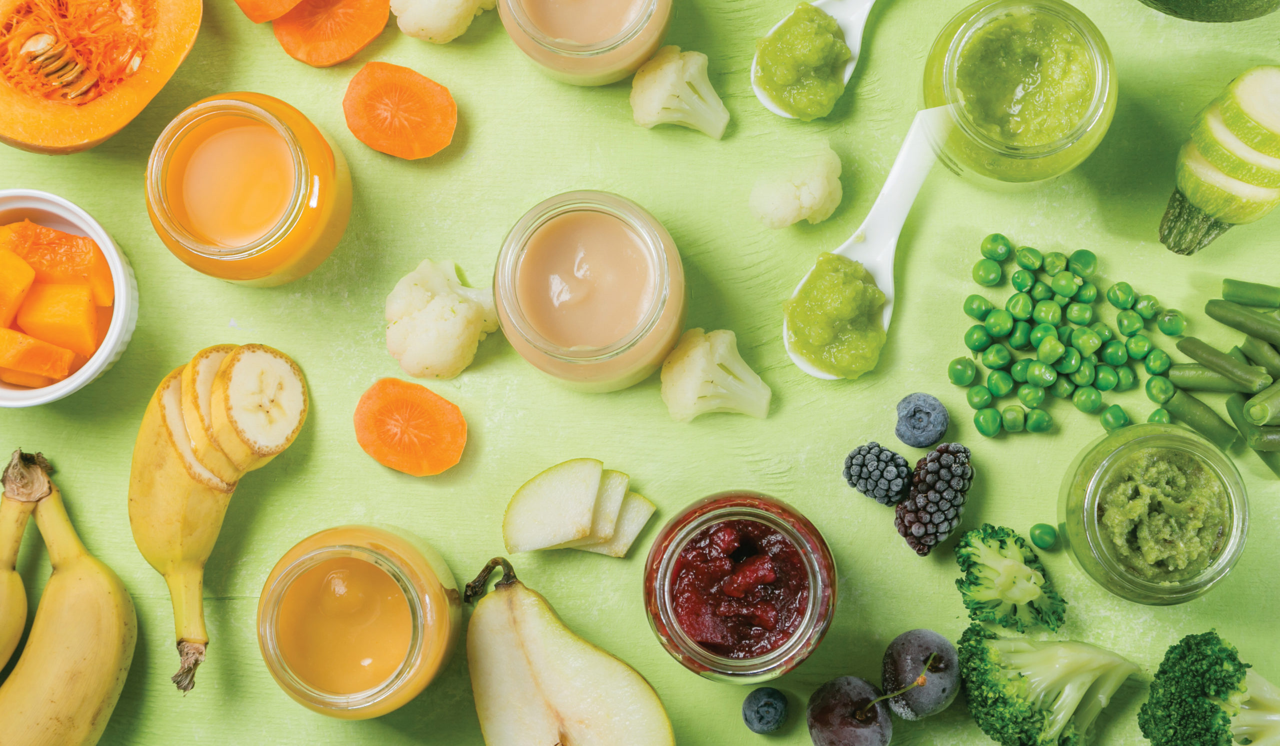 Jars of baby food and cut up bananas, carrots, peas, blueberries, and other colorful vegetables and fruits on a light green background.