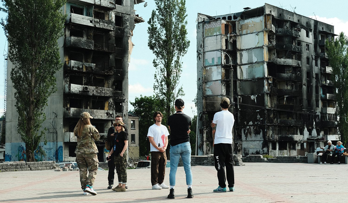 Members of Sunflower Network stand on a concrete area surrounded by blackened and crumbling buildings.